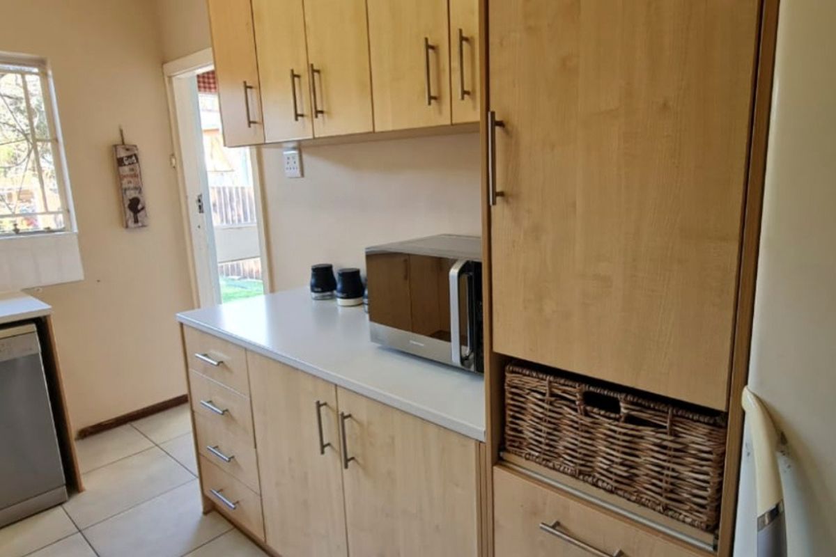A functional kitchen featuring light wood-toned cabinetry, laminate countertops, tiled flooring, and space for integrated appliances with direct access to the exterior.