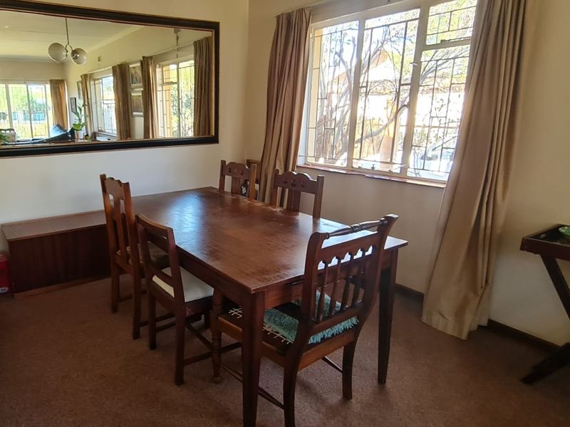 A dining room featuring carpeted flooring and a large window with security bars, providing natural light to the space.