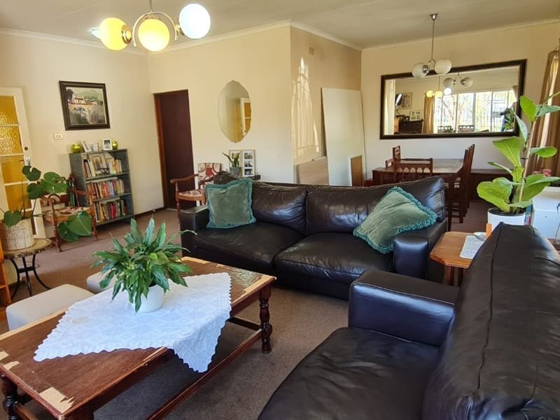 Spacious open-plan living and dining area featuring neutral walls, carpeted flooring, and large windows with security bars.