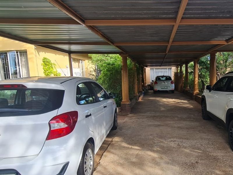 A covered carport area providing sheltered parking with a metal roof structure and concrete driveway.