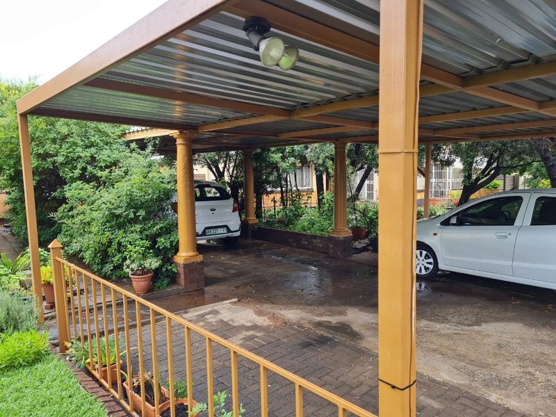 A covered carport area featuring a metal roof structure supported by brick pillars, providing sheltered parking space on a paved driveway.