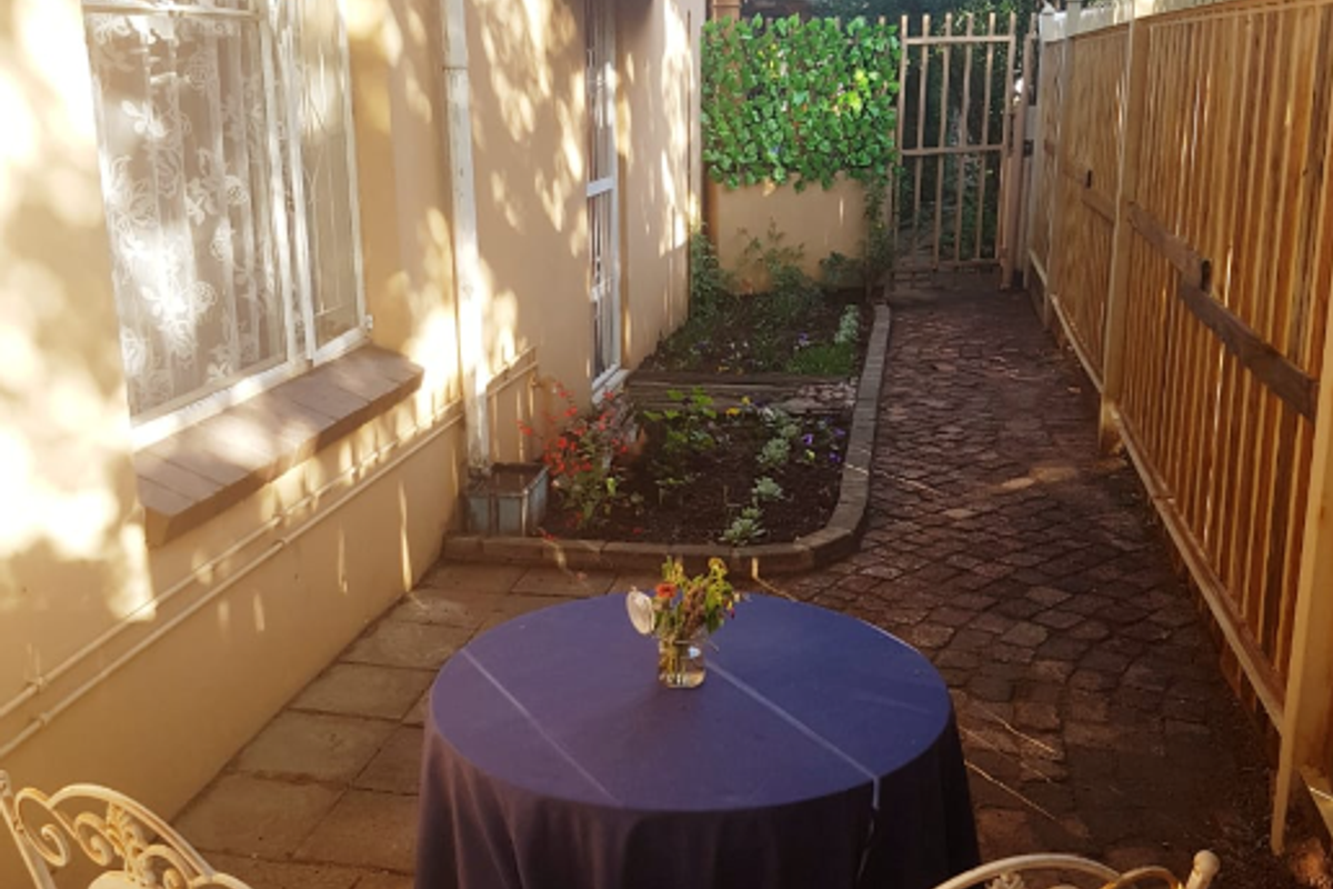 A private rear courtyard featuring paved flooring, a timber boundary fence, a garden bed, and a protective window awning.