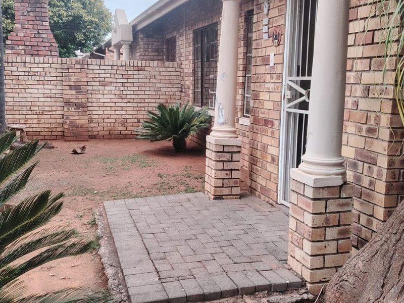 A rear exterior view of a townhouse featuring a paved patio area, brick facade, and a private garden space with boundary walling.