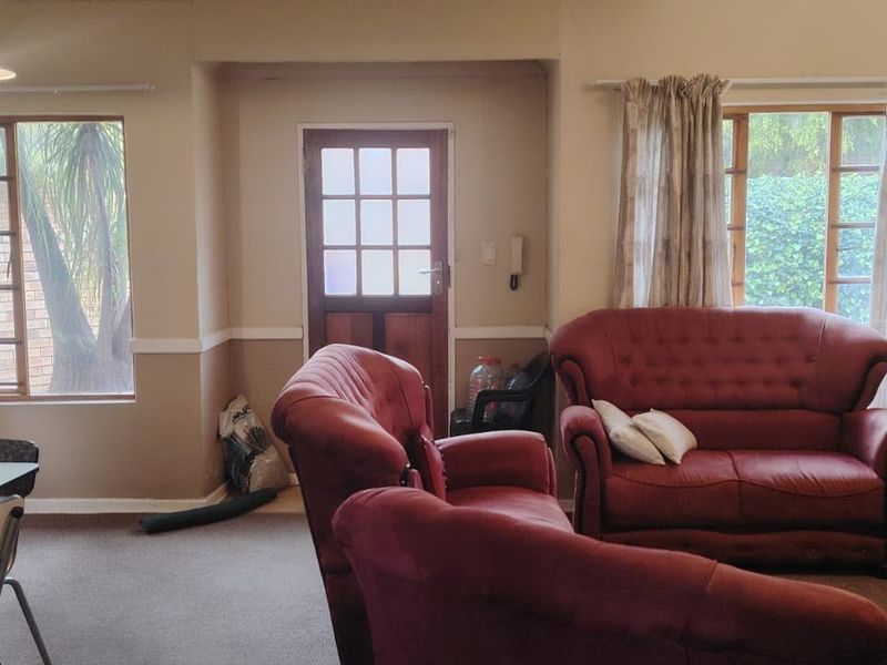 Open-plan living area featuring carpeted flooring, timber-framed windows, and a direct exterior access door, offering a functional layout with potential for modernization.