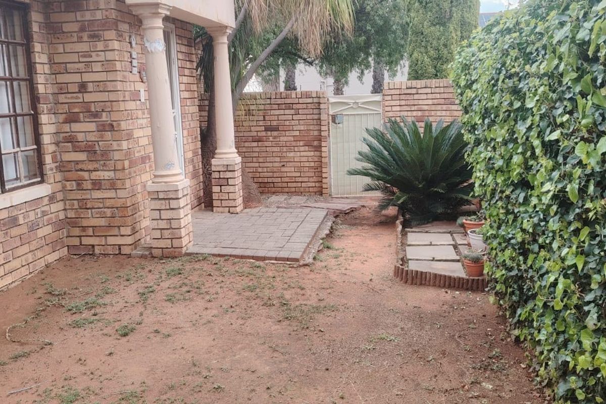 Rear exterior view of a townhouse featuring a brick facade, a small paved patio area, and a private garden space with boundary wall.