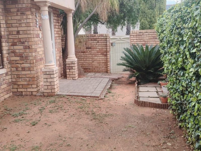 Rear exterior view of a townhouse featuring a brick facade, a small paved patio area, and a private garden space with boundary wall.