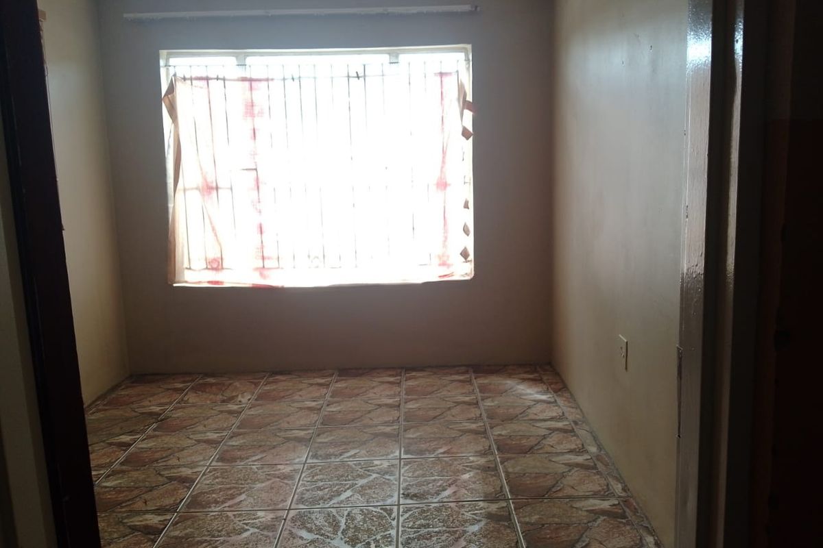 An empty bedroom featuring tiled flooring, security bars on the window, and neutral wall finishes, offering a blank canvas for potential updates.