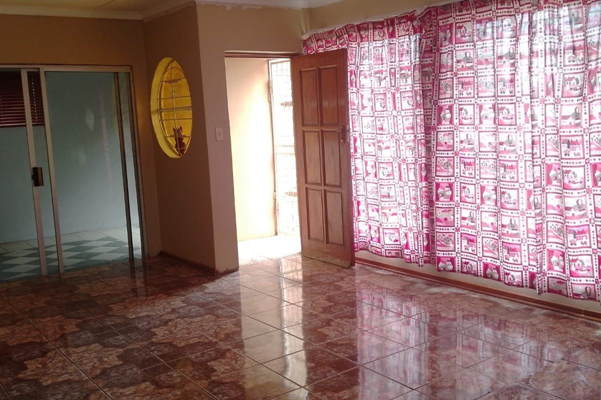 An empty living room featuring tiled flooring, an oval accent window, and access to an adjacent room via a sliding glass door.