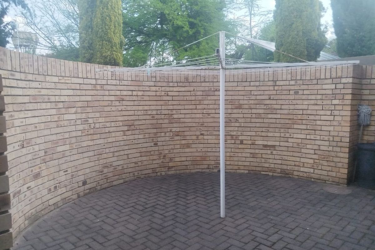 A private rear courtyard area featuring a curved face brick wall and herringbone paved flooring, equipped with a rotary clothesline.