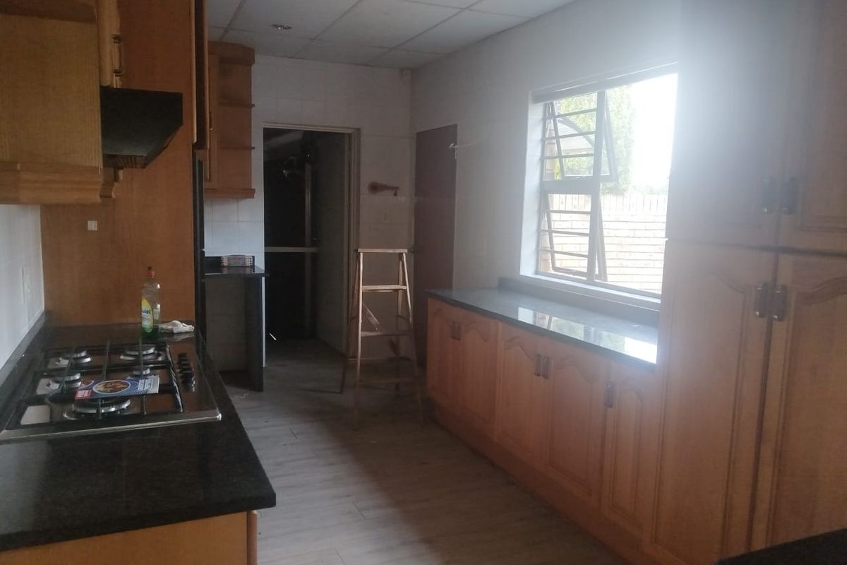 A functional kitchen featuring wooden cabinetry, granite countertops, and a gas hob, offering a practical layout with ample storage space.