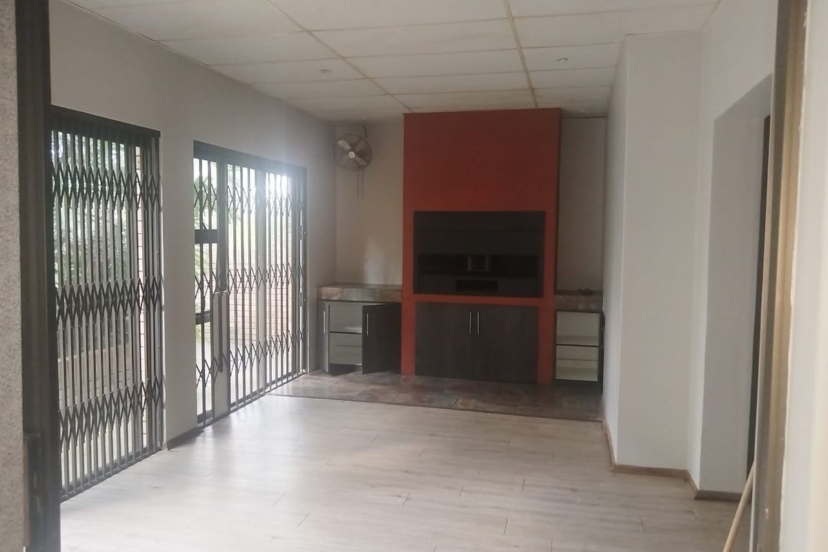 Spacious living area featuring a built-in fireplace with cabinetry, laminate flooring, and sliding doors with security gates leading to the exterior.