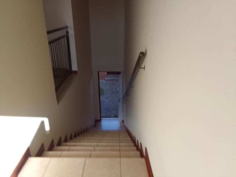 A view looking down a tiled staircase with a metal handrail, leading towards an exterior doorway.