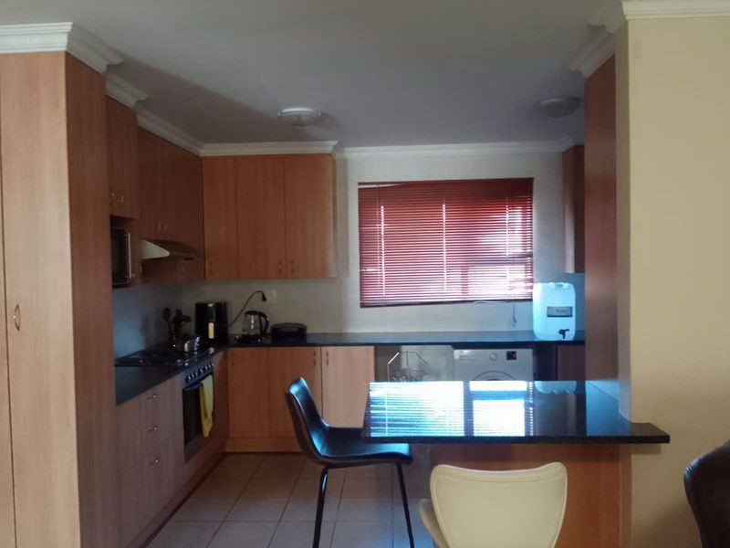 A functional kitchen featuring wood-finish cabinetry, dark countertops, a built-in oven with hob, and a breakfast bar area with tiled flooring.