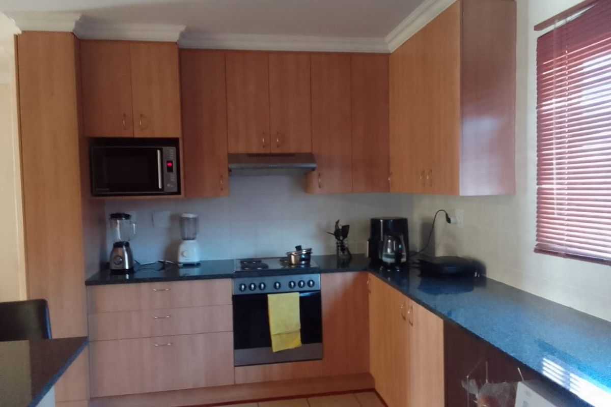 A functional kitchen featuring laminate cabinetry, granite countertops, and built-in appliances including an oven, hob, and microwave.