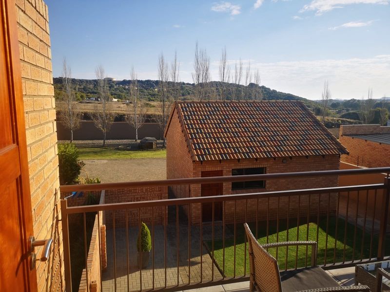 Elevated balcony with metal railing overlooking a private garden, paved courtyard, and a detached brick outbuilding with a pitched tile roof.