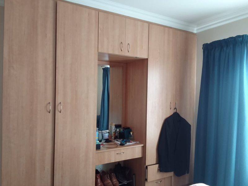 A bedroom featuring extensive light wood-finish built-in cupboards with an integrated vanity desk and mirror, providing ample storage space.