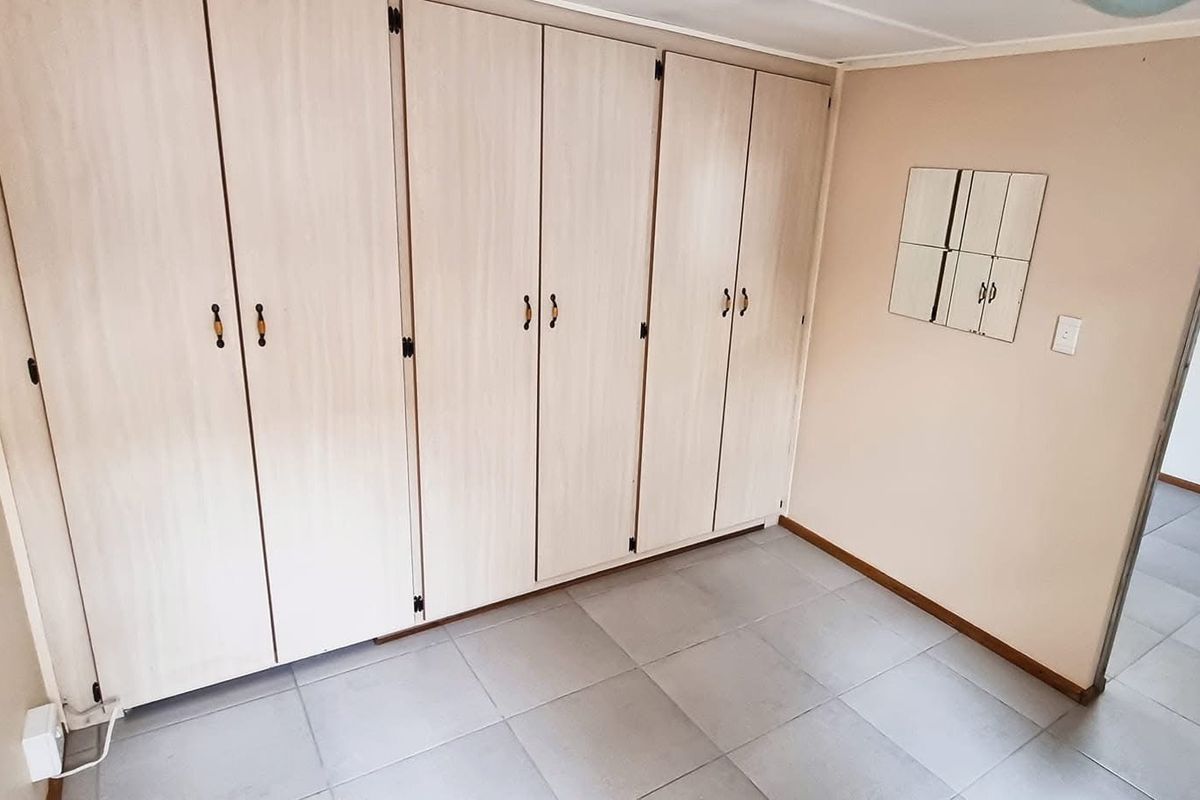 A clean, empty bedroom featuring neutral tiled flooring and extensive built-in wooden cupboards providing ample storage space.