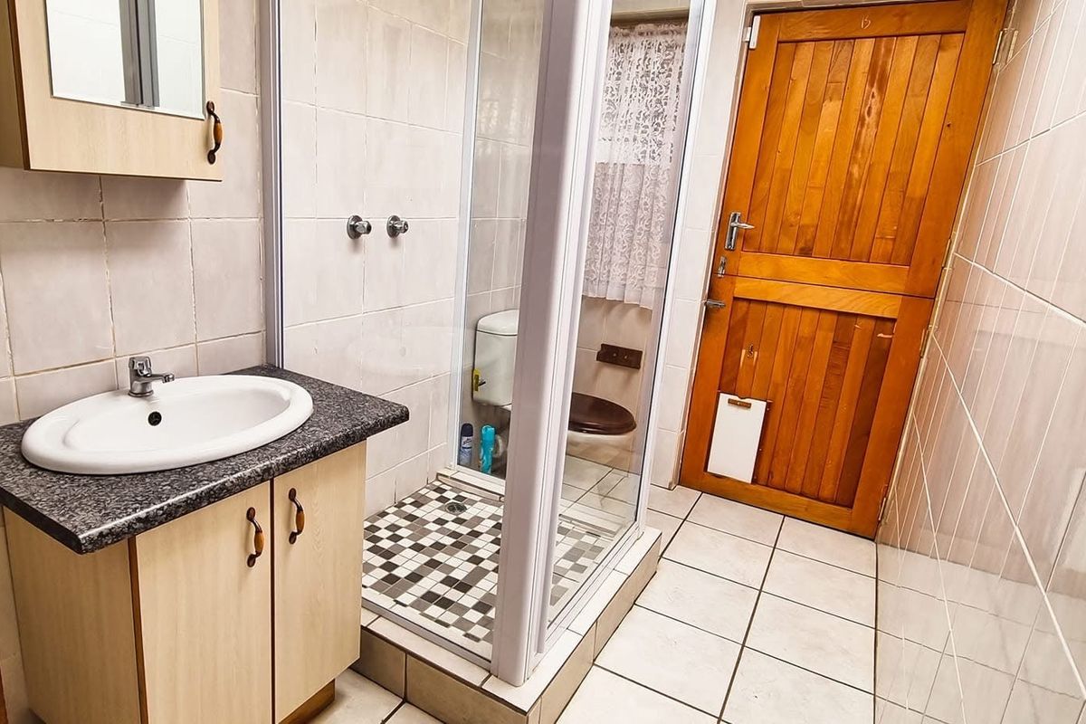 A functional bathroom featuring a vanity unit, shower enclosure, and toilet, finished with neutral wall and floor tiling.
