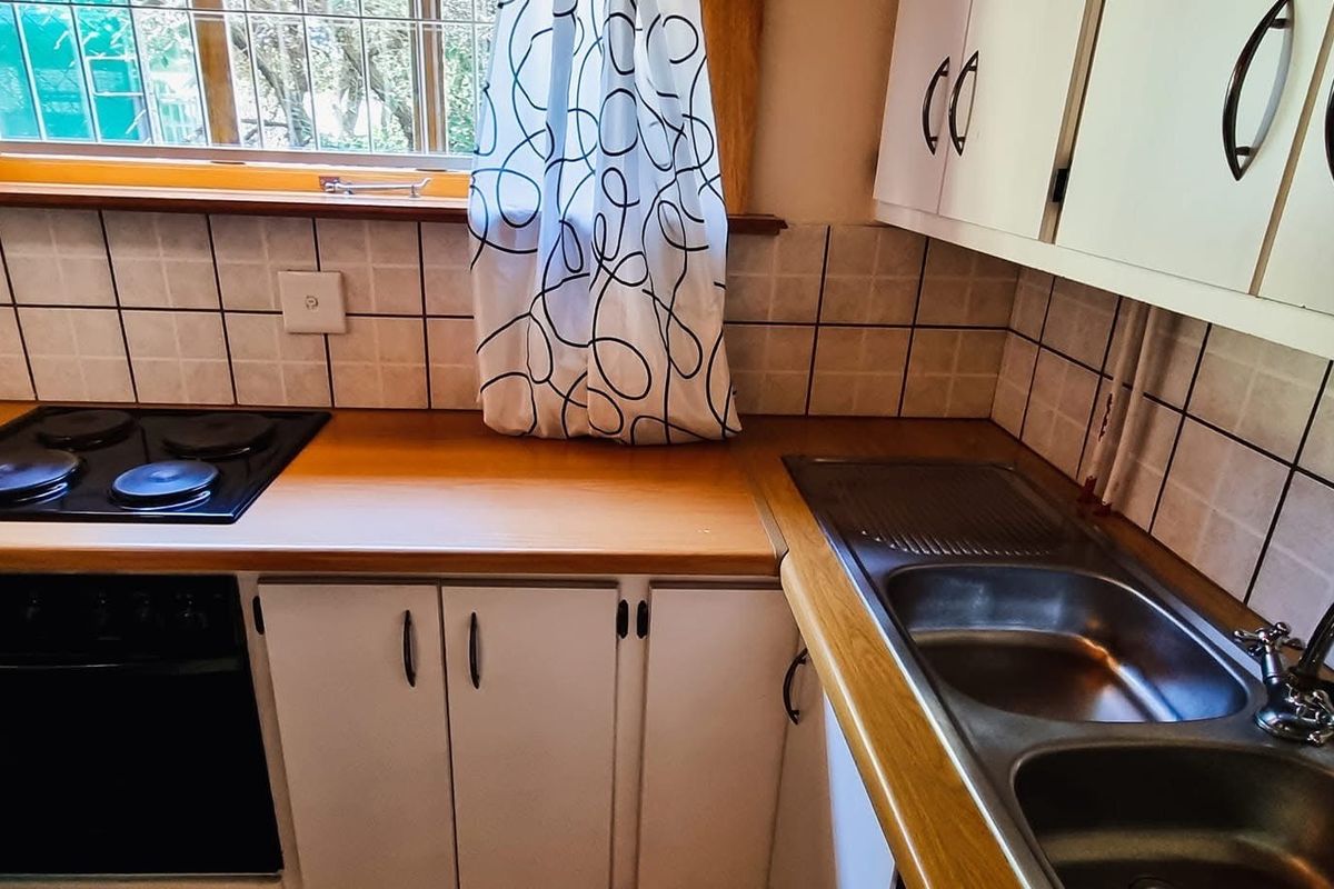 A functional kitchen featuring laminate countertops, a stainless steel double sink, built-in cabinetry, and an integrated electric hob and oven.