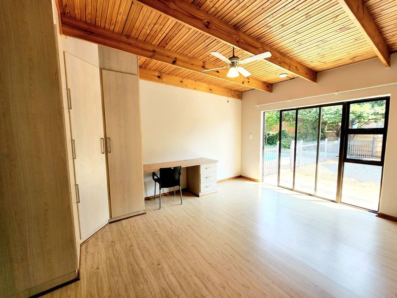 Spacious bedroom featuring exposed timber beam ceilings, built-in cupboards, and large sliding glass doors providing direct access to the outdoor pool area.