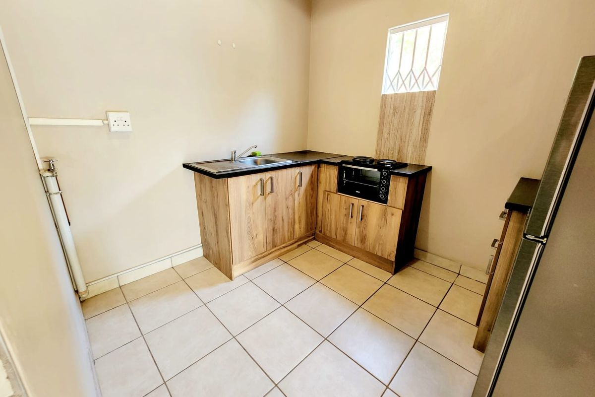 Compact kitchen featuring wood-look laminate cabinetry, built-in oven, hob, stainless steel sink, and tiled flooring.