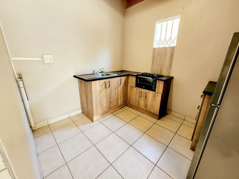 Compact kitchen featuring wood-look laminate cabinetry, built-in oven, hob, stainless steel sink, and tiled flooring.