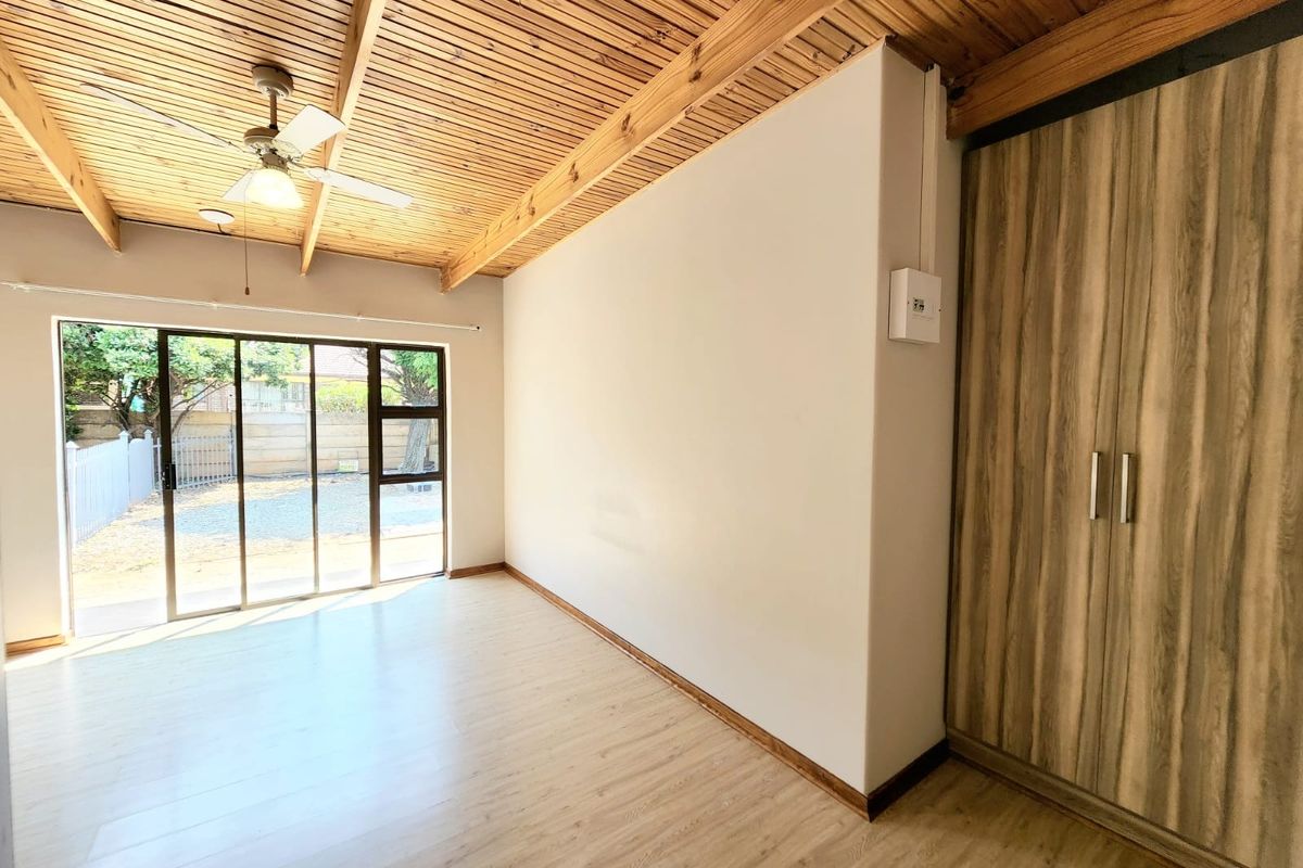 Bright bedroom featuring a unique timber-slat ceiling with exposed beams, built-in wardrobe, laminate flooring, and a sliding glass door leading to the exterior.