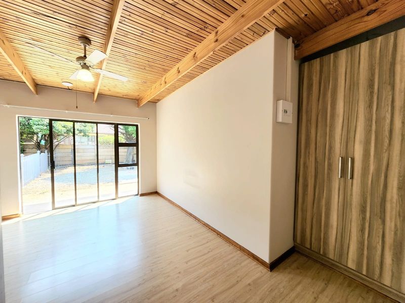Bright bedroom featuring a unique timber-slat ceiling with exposed beams, built-in wardrobe, laminate flooring, and a sliding glass door leading to the exterior.