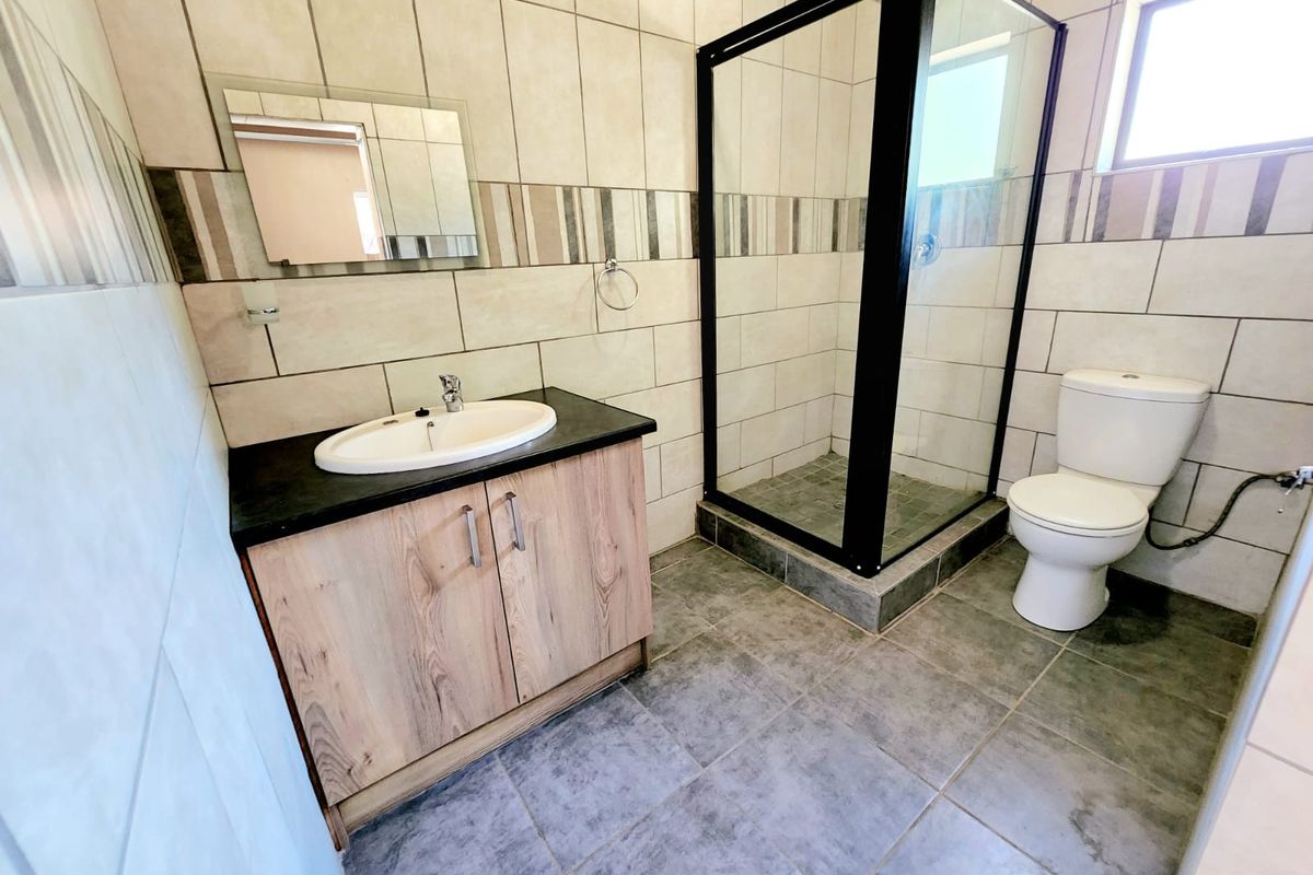 A clean, modern bathroom featuring a vanity cabinet with basin, a glass-enclosed shower, and a toilet, finished with neutral wall and floor tiling.