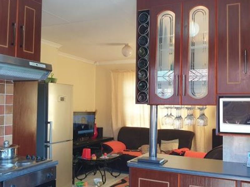 Open plan kitchen and living area featuring dark wood cabinetry, built-in appliances, and a breakfast counter overlooking the lounge space.