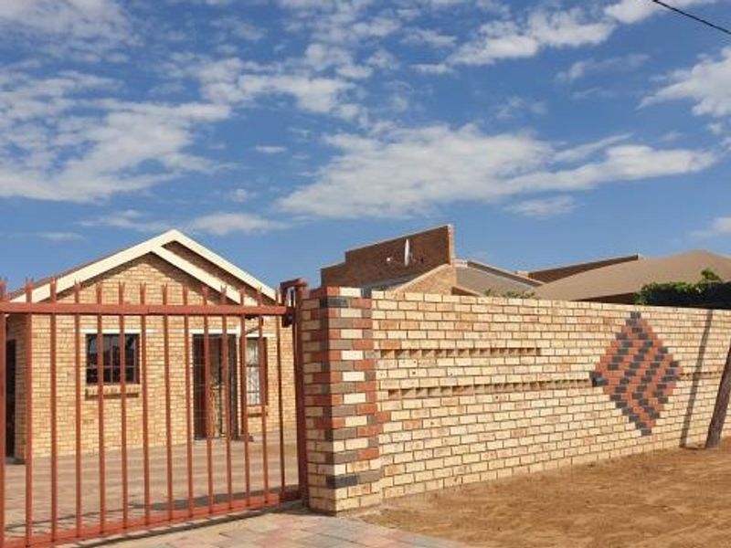 Front view of a face brick house featuring a secure perimeter wall with decorative brickwork and a metal entrance gate.