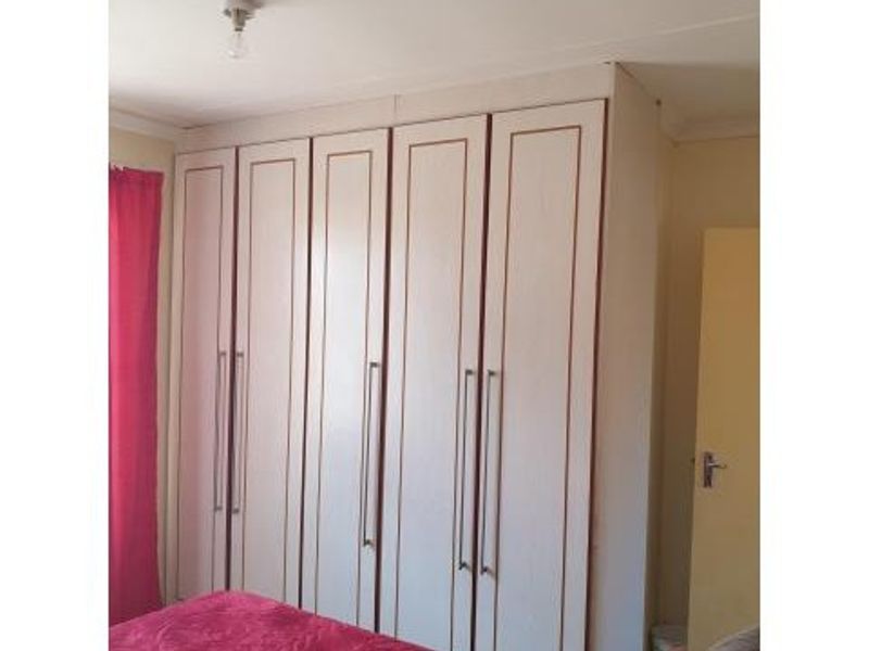 A bedroom featuring floor-to-ceiling built-in cupboards with light wood-grain finish and modern vertical handles.