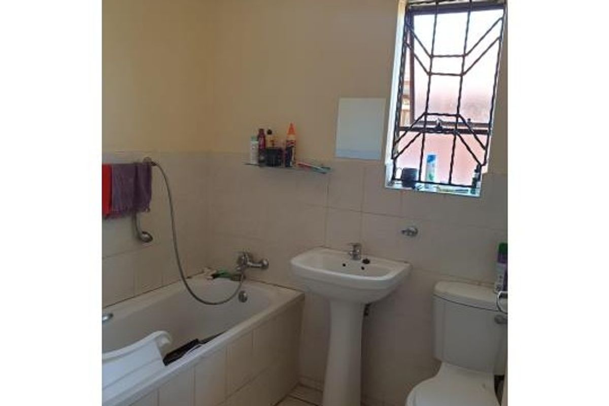 A functional bathroom featuring a pedestal basin, built-in bathtub, and toilet, with tiled wall finishes and security bars on the window.