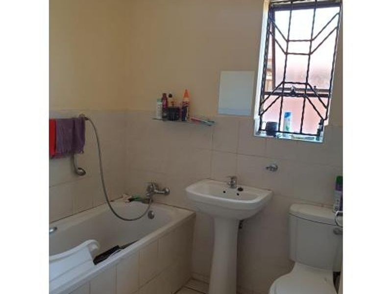A functional bathroom featuring a pedestal basin, built-in bathtub, and toilet, with tiled wall finishes and security bars on the window.