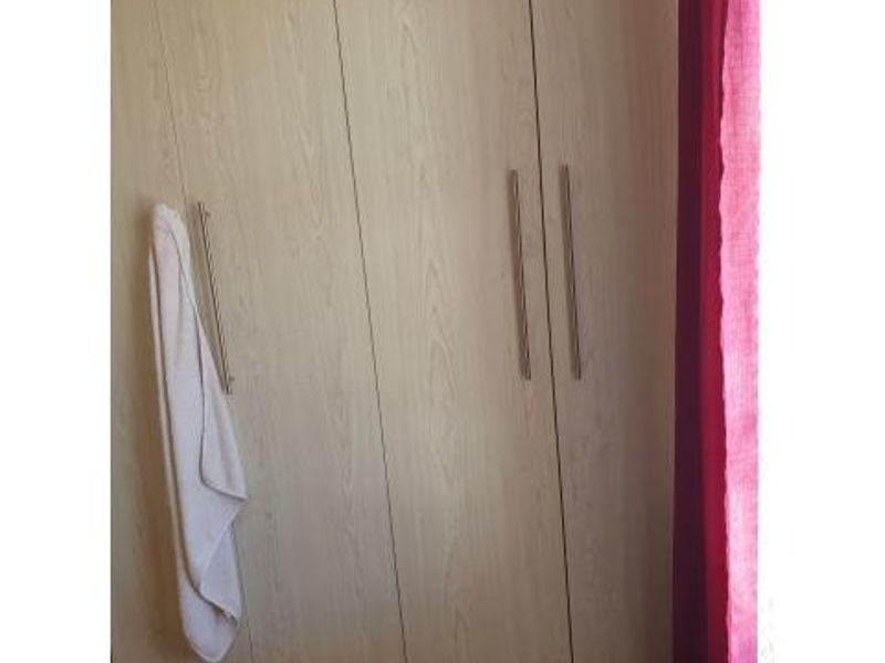 A bedroom featuring light wood-finish built-in cupboards with modern metal handles.