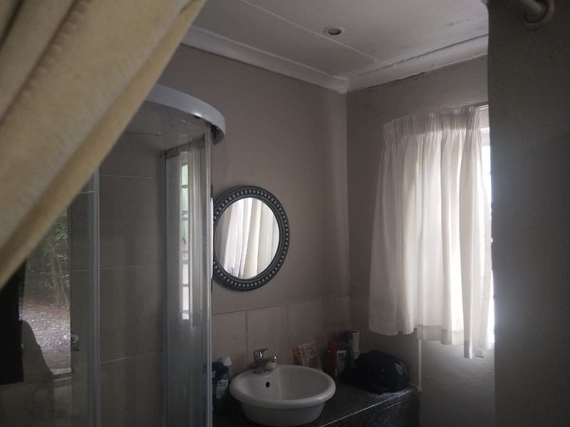 A compact bathroom featuring a shower enclosure and a vanity basin, currently showing signs of wear and requiring cosmetic updates.
