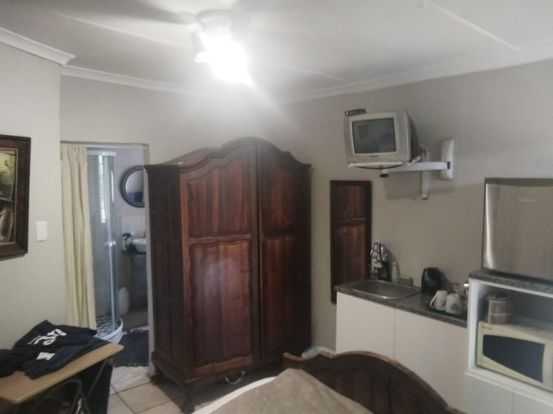 A compact guest bedroom featuring a small kitchenette area with a sink, granite countertop, and an en-suite bathroom.