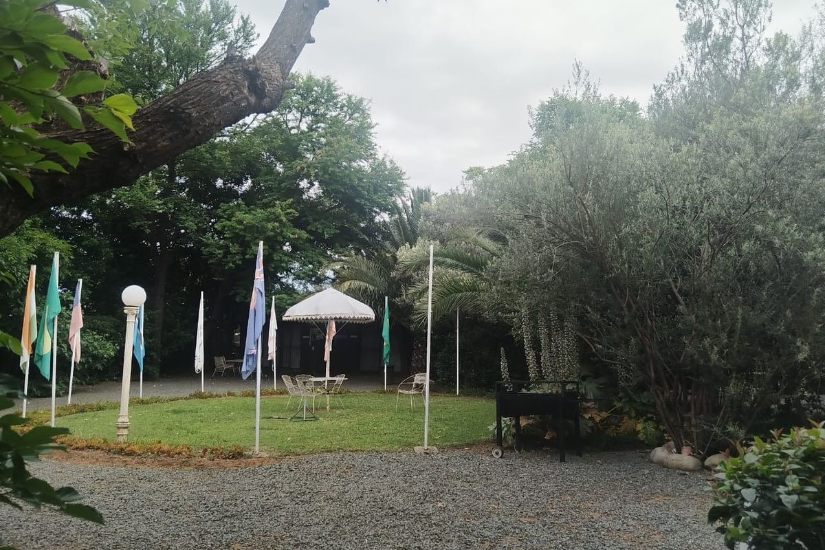 A spacious garden area featuring a gravel driveway, manicured lawn, mature trees, and decorative flag poles, providing a serene outdoor setting.
