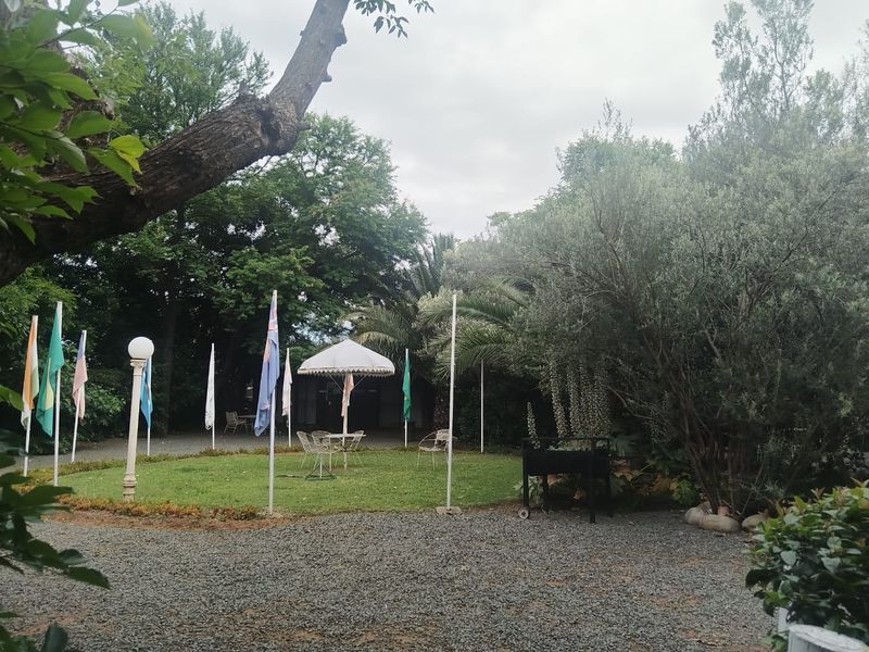 A spacious garden area featuring a gravel driveway, manicured lawn, mature trees, and decorative flag poles, providing a serene outdoor setting.