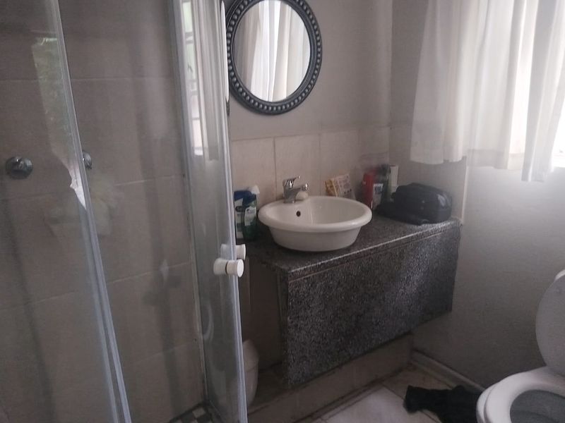 A functional bathroom featuring a vessel sink on a granite vanity, a glass shower enclosure, and a standard toilet.
