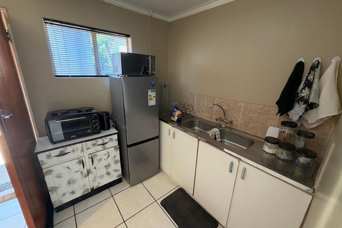A compact kitchen featuring tiled flooring, a stainless steel sink, tiled backsplash, and built-in cabinetry, offering a functional space with potential for modernization.