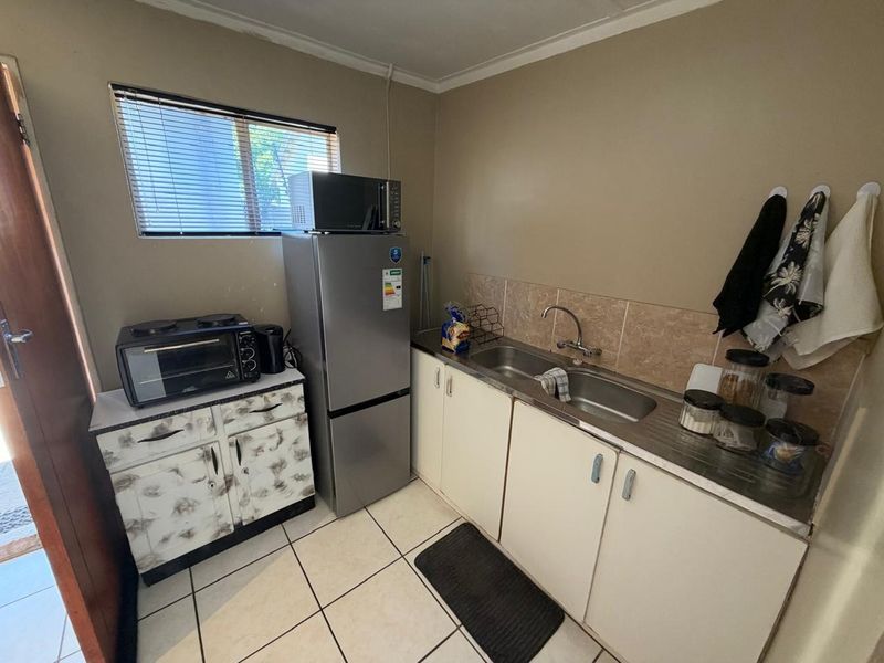 A compact kitchen featuring tiled flooring, a stainless steel sink, tiled backsplash, and built-in cabinetry, offering a functional space with potential for modernization.
