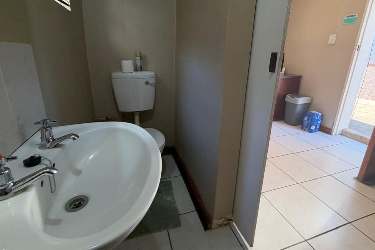 A functional bathroom featuring a pedestal basin and toilet with ceramic floor tiling, showing signs of wear and requiring cosmetic updates.