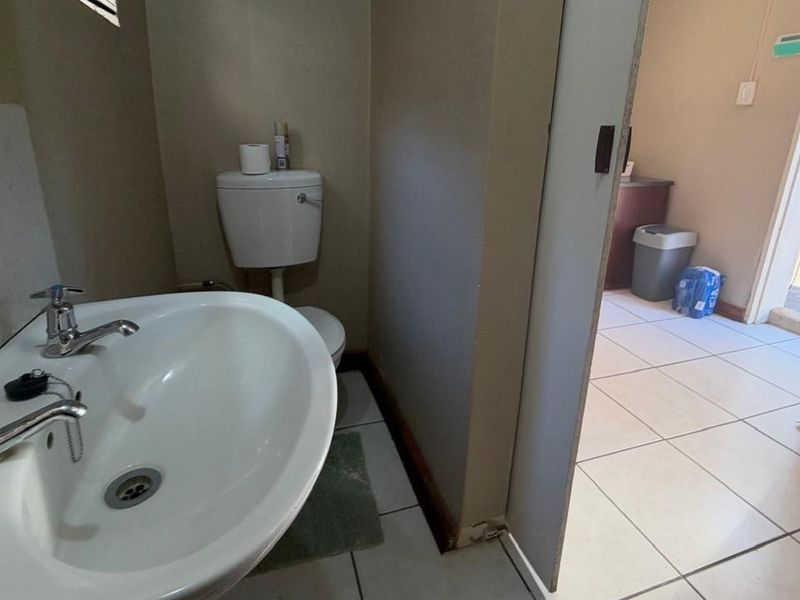 A functional bathroom featuring a pedestal basin and toilet with ceramic floor tiling, showing signs of wear and requiring cosmetic updates.