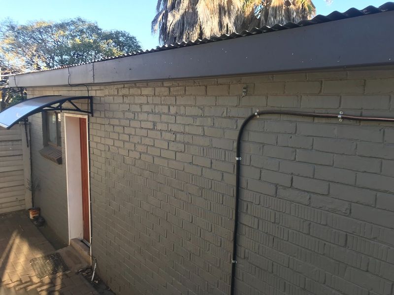 A rear exterior view of the apartment featuring a painted brick facade, corrugated metal roofing, and a paved patio area.