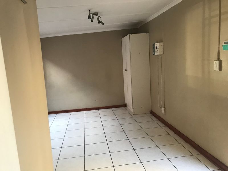 An empty bedroom featuring tiled flooring, a built-in cupboard, and a ceiling-mounted spotlight fixture, requiring minor cosmetic updates.