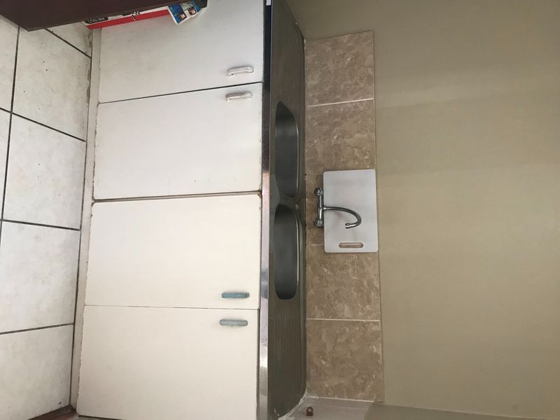 A compact kitchen area featuring a double sink, tiled backsplash, and built-in cabinetry, requiring cosmetic updates to modernize the space.