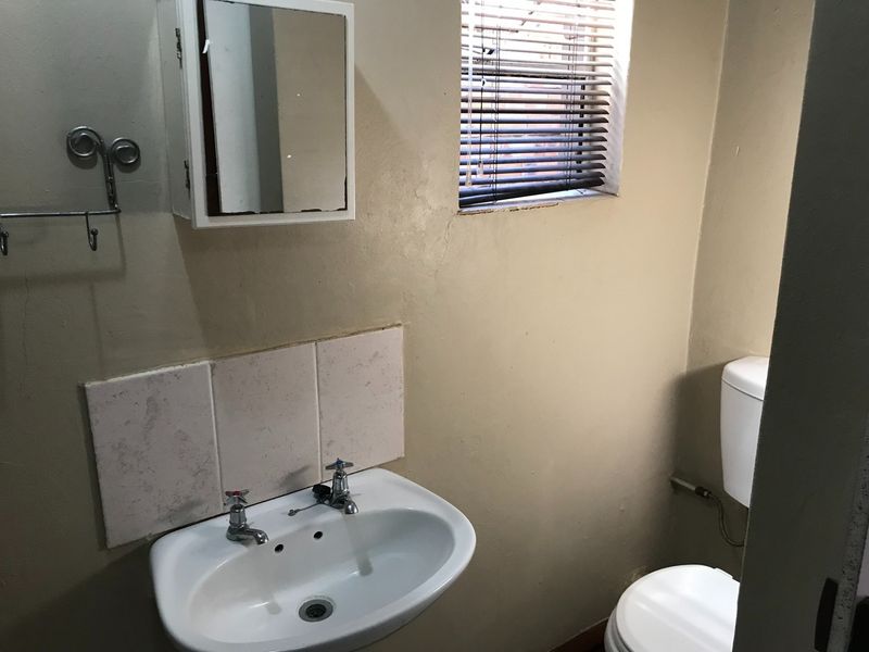 A compact bathroom featuring a pedestal basin with tiled splashback, a wall-mounted medicine cabinet, and a standard toilet.
