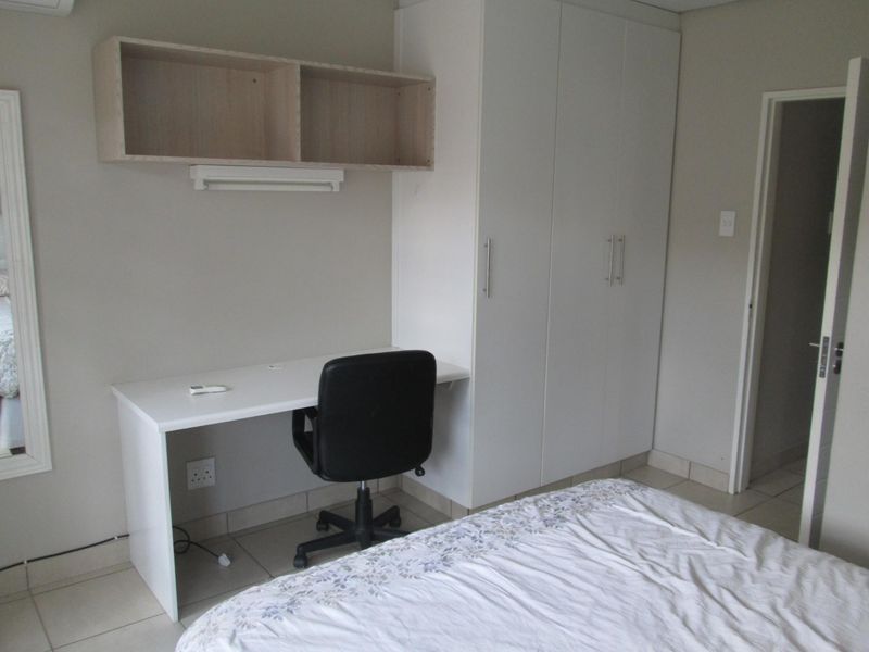 A functional bedroom featuring built-in cabinetry, a desk workspace, wall-mounted shelving, and neutral tiled flooring.