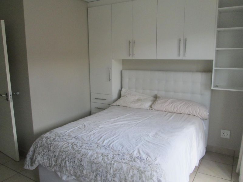 A bedroom featuring white built-in cupboards with integrated shelving and tiled flooring.